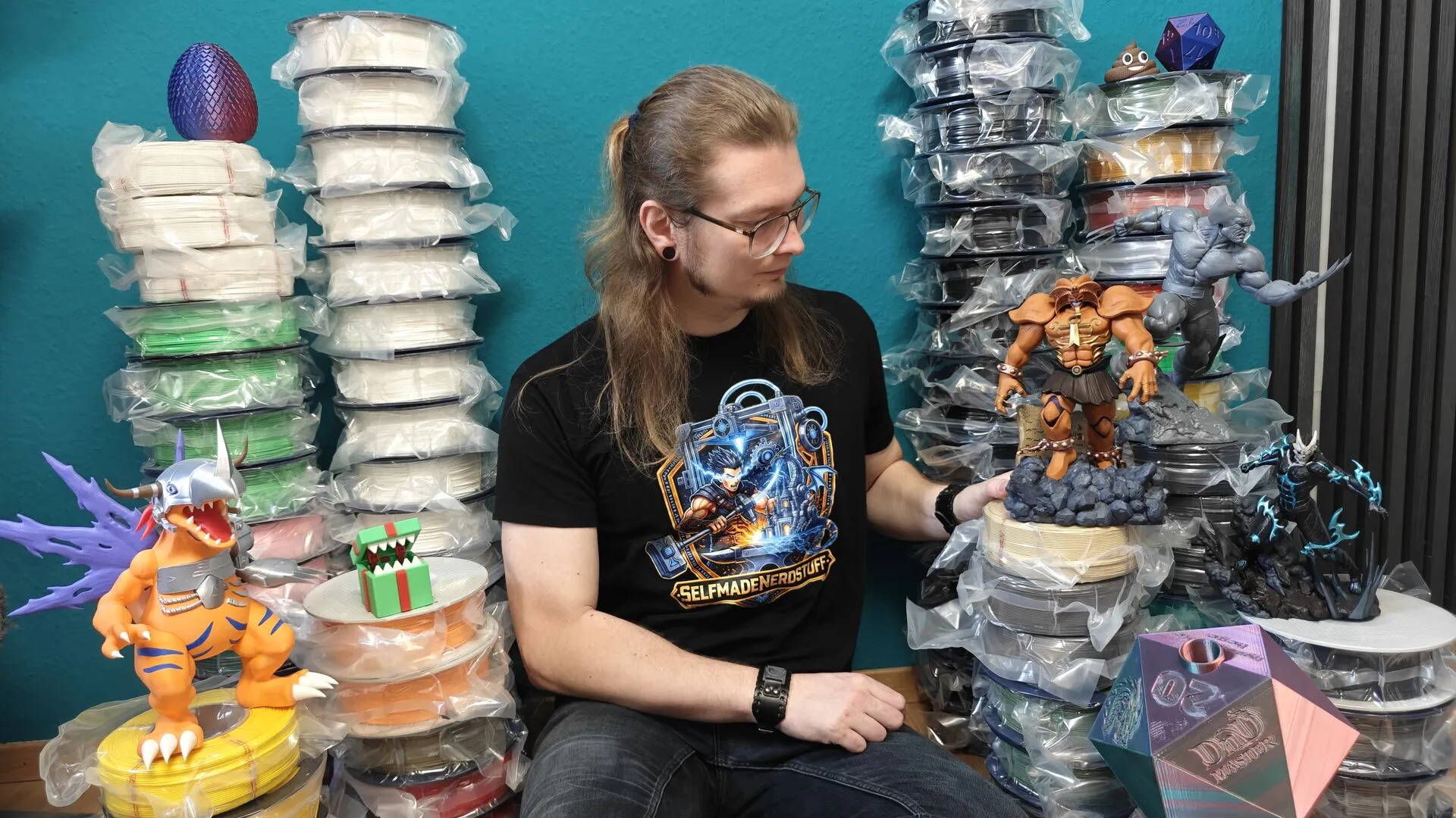 Selbstporträt im Heim-Studio, umgeben von 3D-Druck-Filament-Stapeln und selbst gedruckten Figuren
